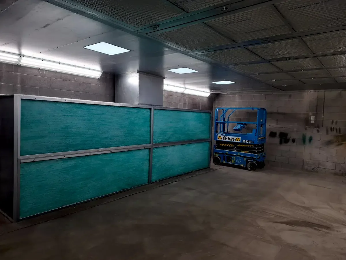 Semi-downdraft spray booth interior at Terex Campsie showing synthetic filter media rear wall and perforated ceiling plenum
